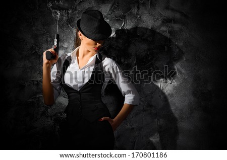 Dangerous and beautiful criminal girl with gun on grey wall