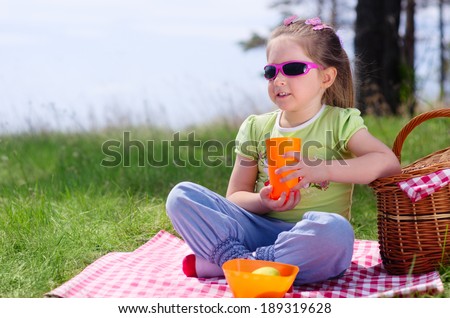 Little girl with picnic basket and plastic cup at lawn