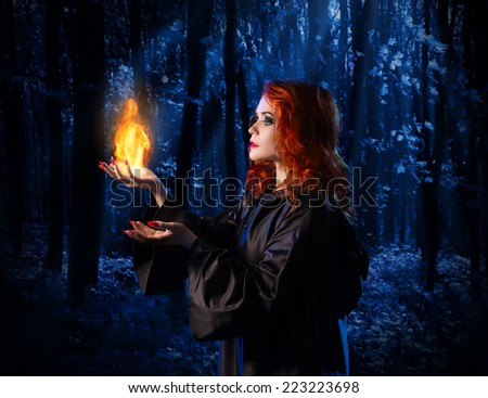 Young witch at night in the moonlight forest with flame