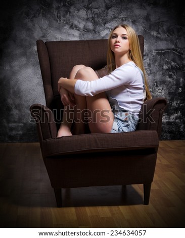 Young girl sit in chair on rough grey wall background