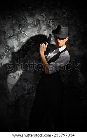 Portrait of young woman in manly style with gun at grey rough wall
