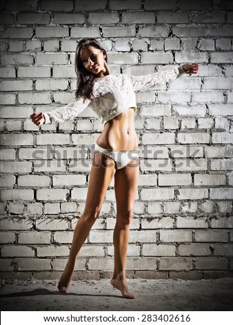 Young dancing woman on grey brick wall background (dark version)