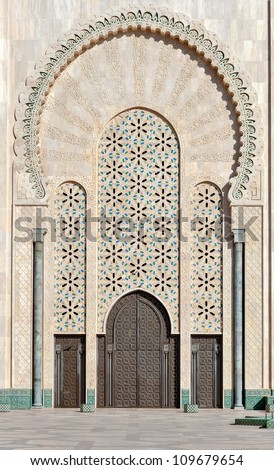 A huge decorated with traditional Arab Islamic ornaments gate. Hassan II Mosque in Casablanca, Morocco. The walls in a light-colored sand, brown wooden door in repeating patterns.