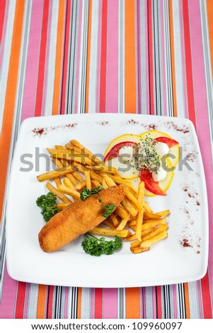 De volaille chop on a plate. The dish of french fries, vegetables, pineapple, parsley, mozarella, tomatoes, sprouts and spices. Plate on the table on a colored background with stripes.