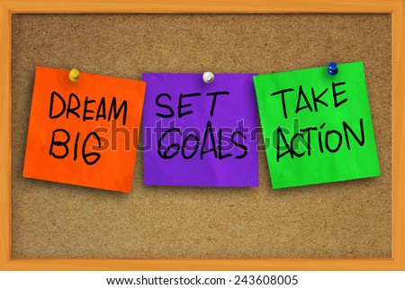 The words Dream Big, Set Goals, Take Action written on sticky colored paper over cork board