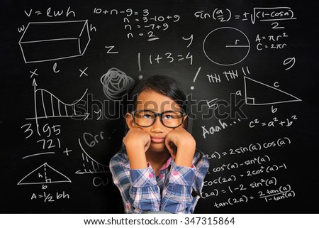 Little Asian student girl with glasses showing bored and tired over green chalkboard with math equivalents written on it