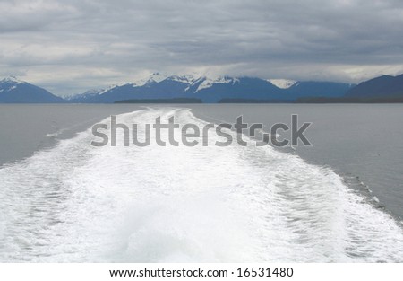 white ships wake under overcast skies with mountains in background.room for copy