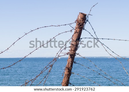 Old barbed wire fence and rusty post against sea and sky