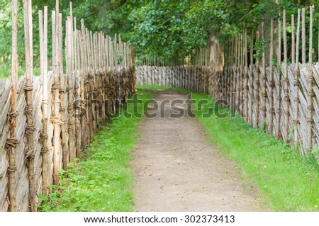Winding walkway between decorative wooden hedges, blurred countryside view
