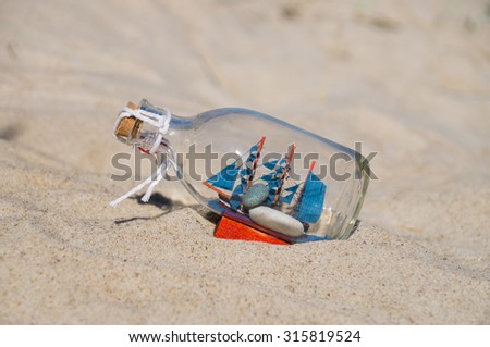 Small ship in the glass bottle lying in the sand, souvenir concept