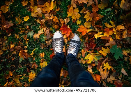 Teenage legs in sneakers and jeans standing on ground with autumn leaves, top view, unusual perspective