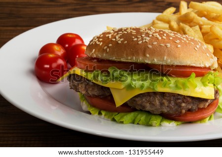 Delicious hamburger stacked high with a juicy beef patty, cheese, fresh lettuce, onion and tomato on a fresh bun with sesame seed standing on  wooden table