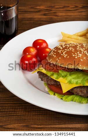 Delicious hamburger stacked high with a juicy beef patty, cheese, fresh lettuce, onion and tomato on a fresh bun with sesame seed standing on  wooden table