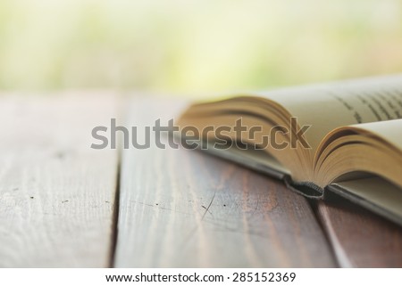 An open book on a rustic wooden table with nature in the background - Split toned