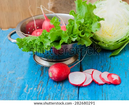 Fresh vegetables, radishes, cabbage, rocket salad on old wooden table in colander