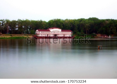 The photo shows house on the river pier on the background of green forest.