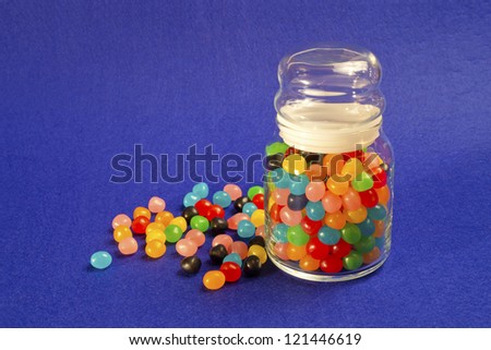 Jar of multicolored Jelly Beans over blue bacground.