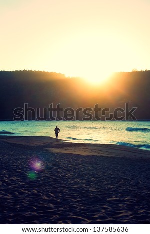 Man in the distance running at sunset on a beach in northern Spain. Cross processing and Flare effect.