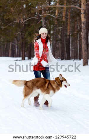 Happy young woman playing with siberian husky dog in winter forest
