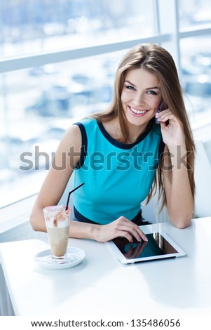 happy young woman talking on the cell phone and using tablet computer in a coffee shop