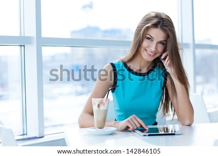 happy young woman talking on the cell phone and using tablet computer in a coffee shop