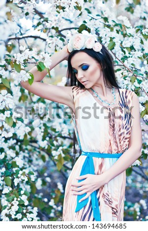 outdoor portrait of a beautiful brunette woman among blossom trees with diadem made of flowers