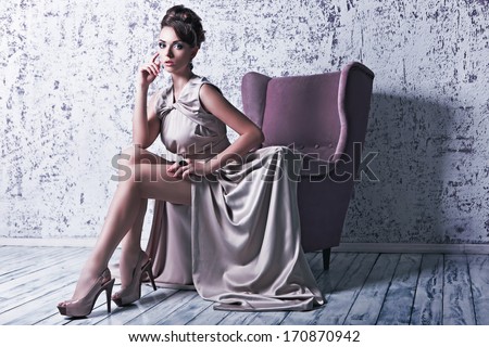 Fashion shot of young beautiful woman in gorgeous silk dress sitting in antique armchair