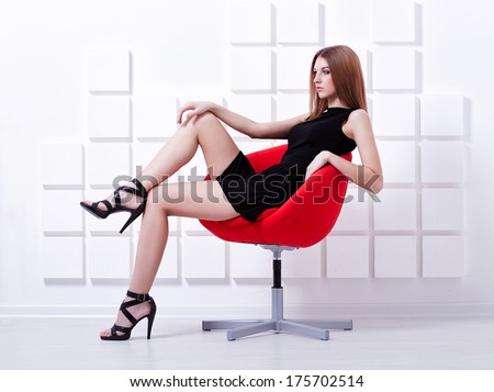Sexy woman in short black dress sitting on a chair. Fashion shot