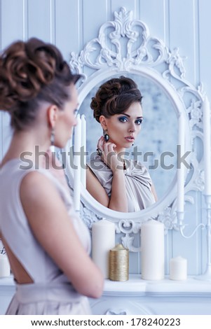 Fashion portrait of young beautiful woman looking in antique mirror, bright makeup and jewelery