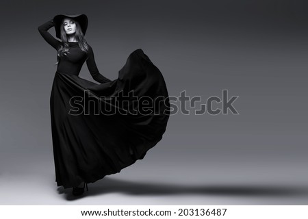 High fashion shot of elegant woman in a hat and long fluttering dress. Black and white image