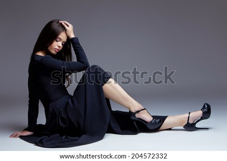 Elegant woman in long black dress sitting on a floor in a studio