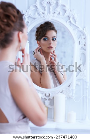 Fashion portrait of young beautiful woman looking in antique mirror, bright makeup and jewelery