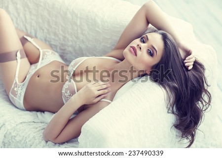 close up portrait of beautiful alluring young woman in white sexy lingerie lying in sofa