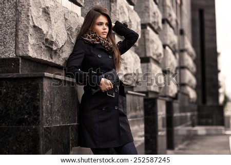 Fashion model with sunglasses, black coat, scarf, and handbag clutch. Outdoor shot