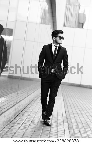handsome stylish man in elegant black suit and sunglasses in the street. Black and white image
