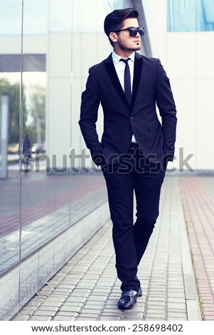 handsome stylish man in elegant black suit and sunglasses in the street