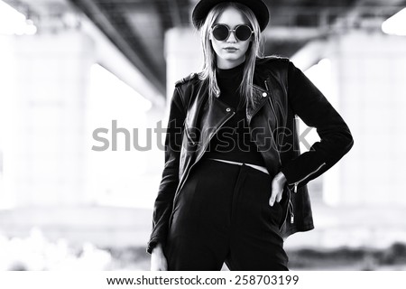 fashion model in sunglasses, hat and black leather jacket posing outdoor. Black and white image