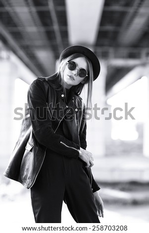fashion model in sunglasses, hat and black leather jacket posing outdoor. Black and white image