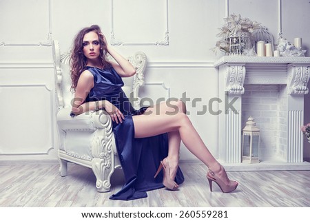 Fashion shot of young beautiful woman in long blue dress sitting in antique armchair