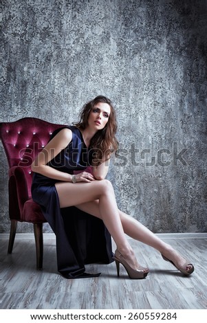 Fashion shot of young beautiful woman in long blue dress sitting in antique armchair