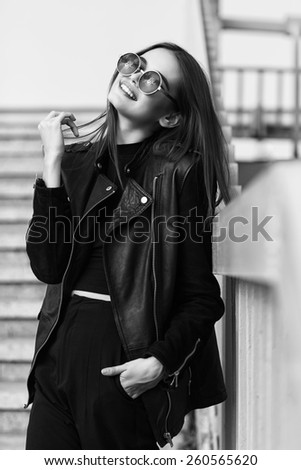 fashion model in sunglasses and black leather jacket posing outdoor. Black and white image