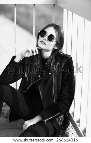 fashion model in sunglasses and black leather jacket posing outdoor. Black and white image
