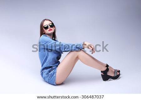 high fashion portrait of young elegant woman in sunglasses and denim overalls, studio shoot
