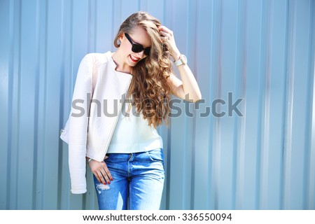 fashion model with long curly hair wearing sunglasses posing outdoor. Jeans, leather jacket.