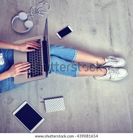 Top view of young woman sitting on floor with laptop, smartphone, tablet computer and notebook