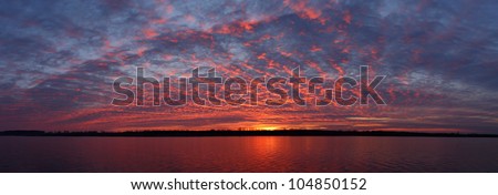 Panoramic view of the Olt river at dusk. The cloud cover turns crimson and reflects on the water surface (Romania, Olt County).