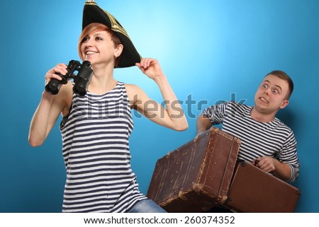 Woman with binoculars in pirate hat, and man with big bags, couple is going on a trip.