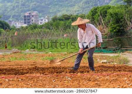 YANGSHUO, CHINA - MAY 01, 2015: A Chinese farmer is working on fields next to Yulong river in Yangshuo. Agriculture is a vital industry in China, employing over 300 million farmers.