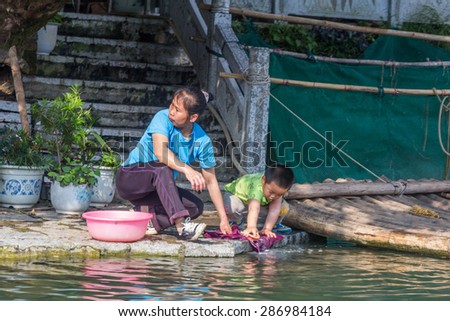 YANGSHUO, CHINA - MAY 01, 2015: A woman and a child washing his clothes next to Yulong river in Yangshuo, China. The Yulong River is a small tributary of the larger Li River.