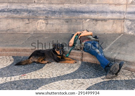LISBON, PORTUGAL - MAY 24, 2015: A homeless person sleeping on the ground with his dog sitting beside him. By Jan 2015, 19.5% of Portuguese population were at risk of poverty after social transfers.